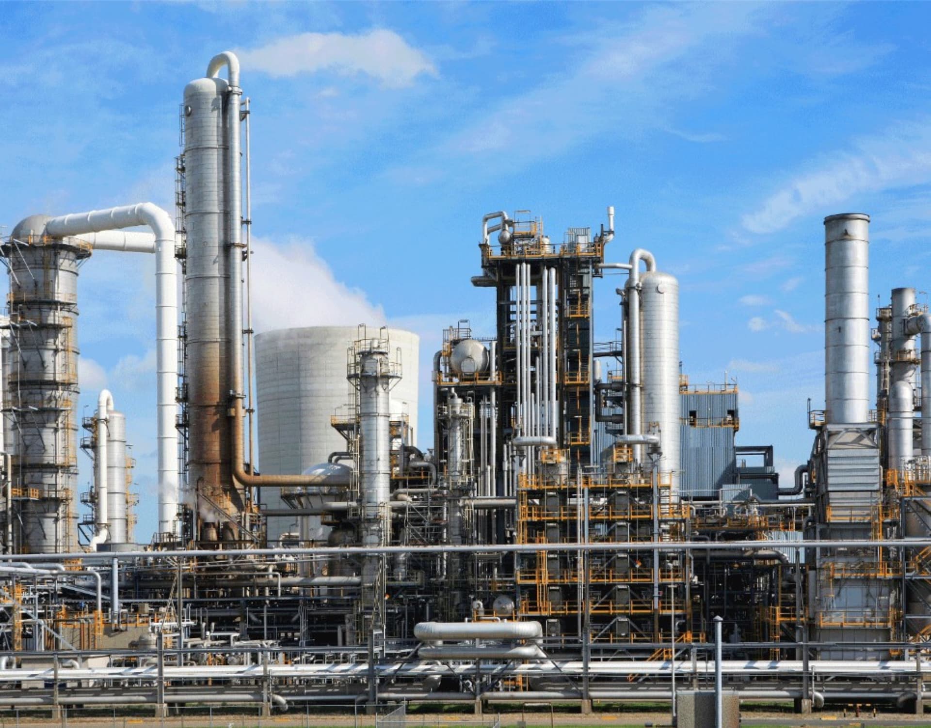Industrial refinery and process plant with columns, insulated piping, and storage under a clear sky