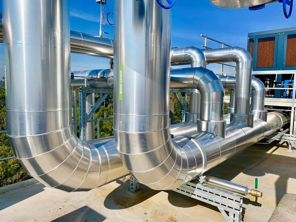 Reflective metal cladding on large insulated pipe elbows on an industrial rooftop