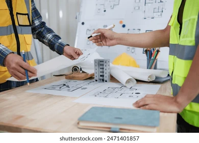 Engineers in hi-vis vests discussing structural plans with blueprints and a building model on the desk